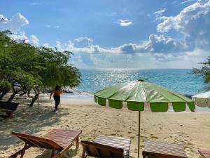a person walking on a beach with an umbrella and chairs at Banthaisangthain Resort in Ko Samed