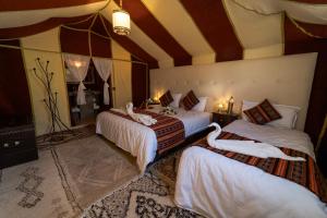 um quarto com 3 camas e lençóis brancos em Sahara Desert Luxury Camp em Merzouga