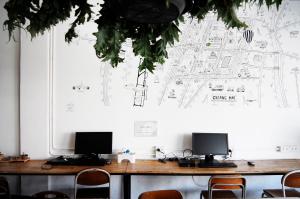 a desk with two monitors on it with a drawing on the wall at Green Sleep Hostel in Chiang Mai