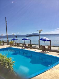 uma piscina com guarda-sóis e cadeiras e o oceano em Apartamento Lexus Beira Mar - apt 101 em Florianópolis