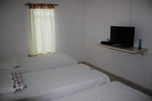 two beds in a room with a television and a window at Pousada Paraíso da Serra in São Raimundo Nonato