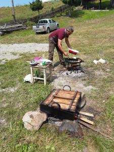 um homem a cozinhar comida num grelhador num campo em Hajnal vendégház em Căpîlniţa