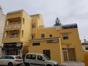 dos coches estacionados frente a un edificio amarillo en Hostal san luis, en San Luis de Sabinillas