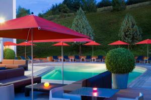 una piscina con sombrillas rojas, mesas y sillas en Hotel Du Golf en Saint-Étienne