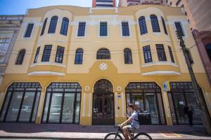 Eine Frau, die vor einem gelben Gebäude Fahrrad fährt. in der Unterkunft Studio Central prox a Rua XV de Novembro - ALL1311 in Curitiba