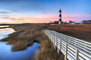 a bridge over a marsh with a lighthouse in the background at 57310 Eagle Pass Rd Home in Hatteras