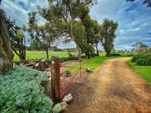 a gate on a dirt road next to a field at Cherry Plum Cottages in Port Fairy