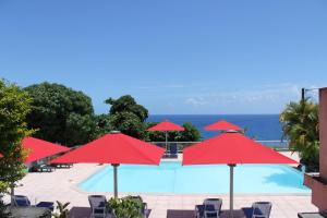 una piscina con sombrillas y sillas rojas y el océano en La Fournaise Hotel Restaurant, en Sainte-Rose