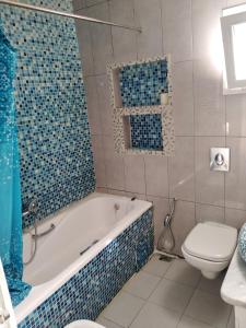 y baño con bañera, aseo y azulejos azules. en Pretty and independent Apartment located in Tunis city, en Túnez