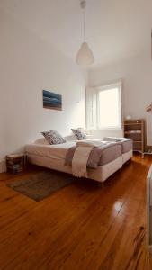 ein großes Bett in einem weißen Zimmer mit Holzböden in der Unterkunft Espinho Guesthouse - Garden House in Espinho