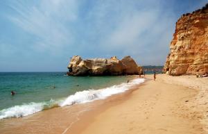 a beach with people swimming in the ocean and rocks at Vila Marachique V Alvor in Alvor