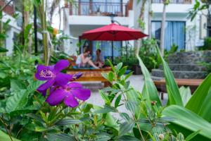 a purple flower in front of a bench and an umbrella at Melica Resort Phu Quoc in Phu Quoc