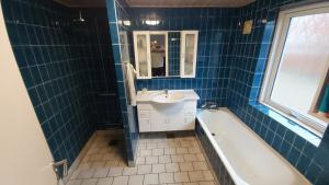 y baño de azulejos azules con lavabo y bañera. en Landsted med aktivitethal, en Karby