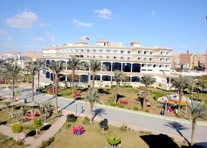 a large white building with palm trees and a street at Elminya Compound in Al Minya