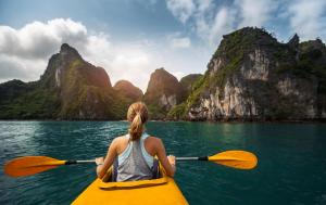 Una donna in kayak in acqua con le montagne di Madeline Cruises a Ha Long