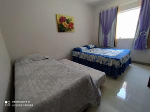 2 Betten in einem Zimmer mit lila Vorhängen und einem Fenster in der Unterkunft Casa de Praia Lado Sul in Guriri