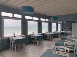 a dining room with tables and chairs and the ocean at Hôtel La Sirène in Yport