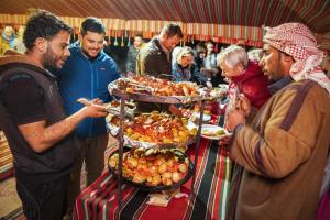 grupa ludzi stojących przy stole z jedzeniem w obiekcie Mohammed Mutlak Camp w mieście Wadi Rum