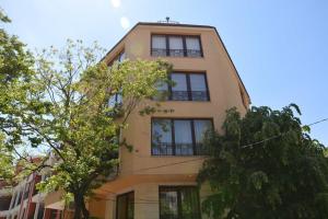 a tall yellow building with windows and trees at Vazov Residence , two bedroom top centre apartment in Varna City