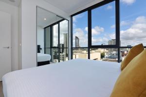 a bedroom with a white bed and large windows at Hope Street Apartments by CLLIX in Brisbane