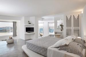 a white bedroom with a large bed and a tv at Suites of the Gods Cave Spa Hotel in Megalokhori