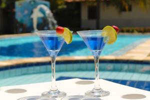 two martini glasses with fruit on a table near a swimming pool at Village Miramar in Maragogi