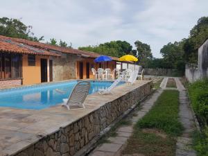 a pool with chairs and umbrellas next to a house at Pousada Solar Tropical in Saquarema