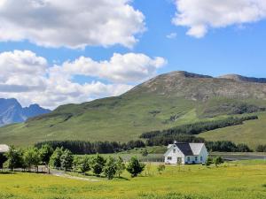 a white house in a field with mountains in the background at Holiday Home Strath Glebe by Interhome in Broadford