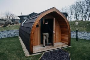 a man is standing inside of a small wooden iguanauanauanauanauanauana at North Coast 500 Pods in Achmelvich