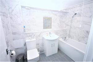 a white bathroom with a sink and a toilet and a tub at The Aldgate Rooms in London