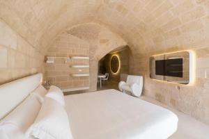 a bedroom with a white bed and a tv at Aquatio Cave Luxury Hotel & SPA in Matera
