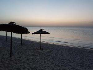 two straw umbrellas on a beach with the ocean at Royal Thalassa Monastir in Monastir
