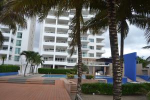 a large white building with palm trees in front of it at Suite frente al mar Playa Azul in Tonsupa