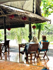 dos mujeres sentadas en sillas bajo un paraguas en Lakeside Homestay, en Hoi An