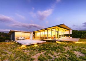 ein modernes Haus mit Glaswänden und einer Terrasse in der Unterkunft Cloudy Bay Beach House in South Bruny