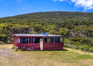 a red caravan with a surfboard on top of a hill at Cloudy Bay Cabin in South Bruny
