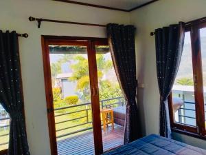a bedroom with a bed and a balcony with a window at Thanorm Rak Resort in Khao Kho