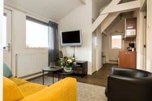 een woonkamer met een gele bank en een tv bij Appartementen Parkzicht in Bergen aan Zee