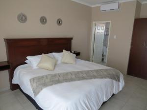 1 dormitorio con 1 cama grande con sábanas y almohadas blancas en Villa Strada Guesthouse, en Klerksdorp