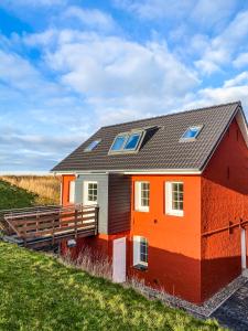 une maison orange avec un toit noir sur un champ dans l'établissement Ferienhaus Südwesthörn, à Emmelsbüll-Horsbüll