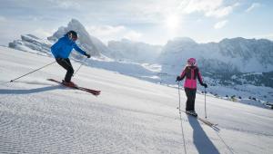 two people are skiing down a snow covered slope at Adler Spa Resort Dolomiti in Ortisei