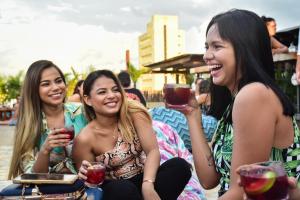 three women laughing while holding wine glasses at La Brisa Loca Hostel in Santa Marta