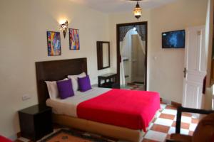 a bedroom with a bed with a red blanket and purple pillows at Hotel Cap Sim in Essaouira