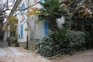 a white house with blue windows and a palm tree at Apartments Sabadin in Portorož