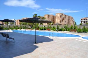 una piscina con due ombrelloni e una panchina accanto ad essa di Apartamentos Marina Park a Oropesa del Mar