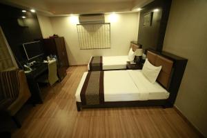 a bedroom with two beds and a desk and a television at Hotel Comfotel Kolkata in Kolkata