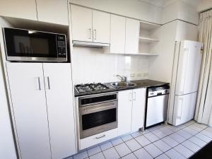 Il comprend une cuisine blanche équipée d'une cuisinière et d'un four micro-ondes. dans l'établissement Inn on the Park Apartments, à Brisbane