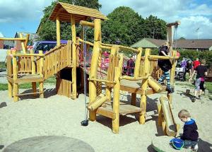 a young boy sitting in front of a wooden playground at Nørager Apartments in Nørager