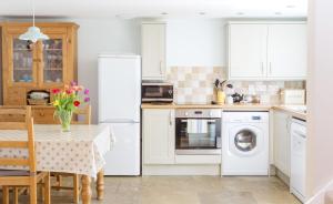 a kitchen with white appliances and a table with flowers on it at See the llamas at a beautiful Somerset Cottage in Combe Saint Nicholas