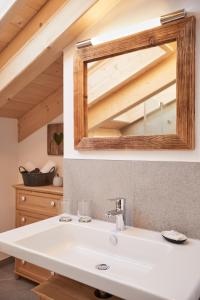 La salle de bains est pourvue d'un miroir au-dessus d'un lavabo blanc. dans l'établissement Landhaus Herzogsteig, à Krün